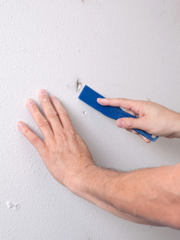 man-filling-in-holes-and-gaps-on-textured-wall-with-putty-knife-for-painting-preparation