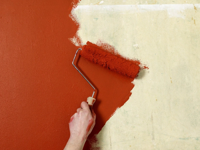 roller-brush-painting-clay-red-paint-over-textured-wall