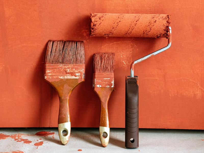 paint-brushes-and-paint-roller-in-rust-oarange-paint-leaning-against-rust-orange-wall