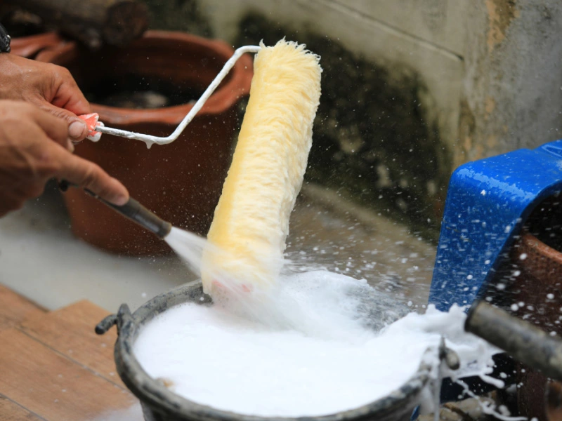 paint-roller-being-cleaned-off-by-a-hose-and-bucket-of-soapy-water-cleaned