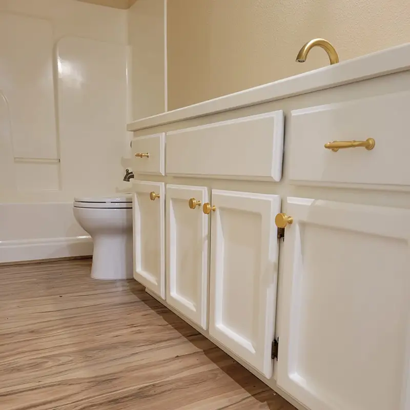 bathroom-with-white-painted-cabinets-gold-sink-wood-floors-and-beige-walls