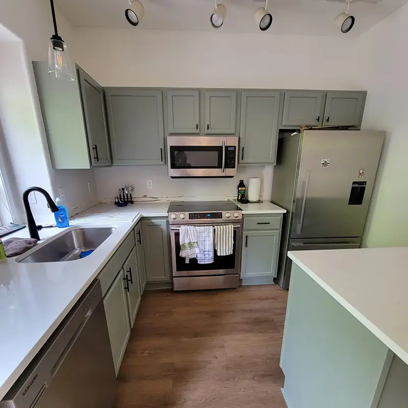 kitchen-with-metal-appliances-green-cabinets-and-white-walls-and-countertops